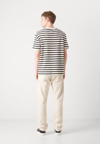 Striped t-shirt in cream and navy, featuring a round neckline and short sleeves, paired with light beige pants and dark shoes.