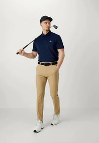 Camisa polo azul-marinho com colarinho, calças cáqui, cinto preto e ténis brancos. Segurando um taco de golfe, usando uma chapéu preto. Design simples.