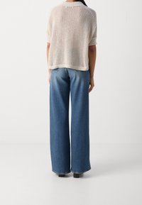 Lekki, kremowy sweter z dzianiny o luźnym kroju i krótkich rękawach. Połączony z wysokimi, szerokimi spodniami dżinsowymi w kolorze niebieskim.