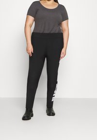 Svarta leggings med ett stretchigt midjeband och logodetalj i vitt på sidan. Toppdelen är en figurnära grå t-shirt med kort ärm.