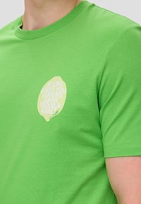 Grünes Baumwoll-T-Shirt mit kurzen Ärmeln, Rundhalsausschnitt und einer limettengrünen Grafik mit einem textbasierten Zitat auf der Vorderseite.