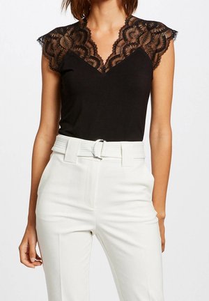 Zwarte top met kant kapmouwen, V-halslijn; gecombineerd met hoog-getailleerde witte broek met een leren riem met zilveren gesp. Soepele stoftextuur.