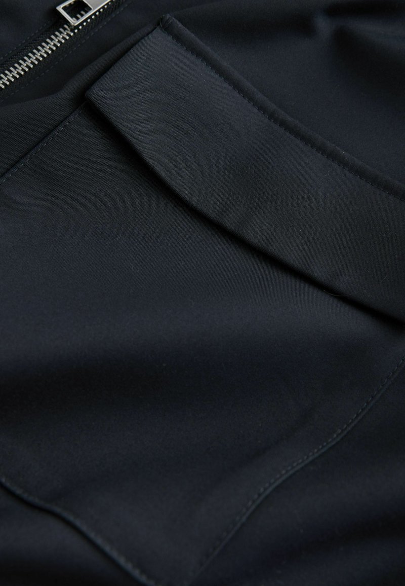 Black fabric featuring a smooth, matte texture with a zip detail and a folded pocket. Seam lines are visible.