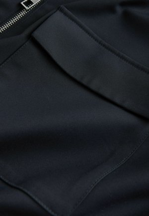 Zwarte stof met een gladde textuur, voorzien van een zak en een zichtbare metalen rits. Eenvoudig ontwerp met minimale stikdetails.