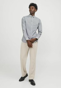 Camicia button-up di colore azzurro chiaro con un motivo geometrico, maniche lunghe e collo. Abbinata a pantaloni beige e scarpe nere.