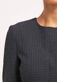 Abito blu navy in tessuto testurizzato con un motivo sottile, scollatura rotonda e spalle strutturate, che mette in mostra un design elegante e aderente.