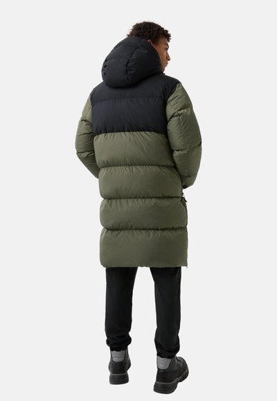 Puffer coat with a black upper section and olive green lower section. Features a hood and vertical stitching, paired with black pants and shoes.