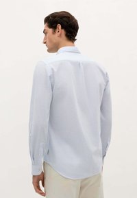 Camicia a righe blu chiaro con colletto classico, maniche lunghe e orlo curvo. Il tessuto ha una texture liscia, con polsini abbottonati e etichette laterali.