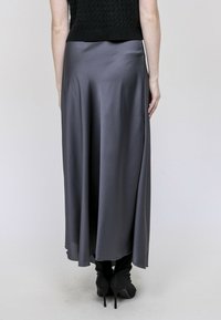 Jupe longue et fluide en satin gris, présentant une texture lisse et un ourlet qui tombe élégamment sous les genoux. Portée avec des talons hauts noirs.