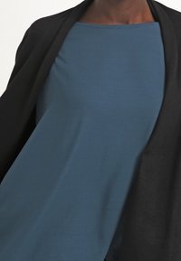 Modrý top s krátkým rukávem spárovaný s černým kardiganem s otevřeným předním dílem. Top má jednoduchý design a hladkou texturu. Kardigan má měkký povrch.