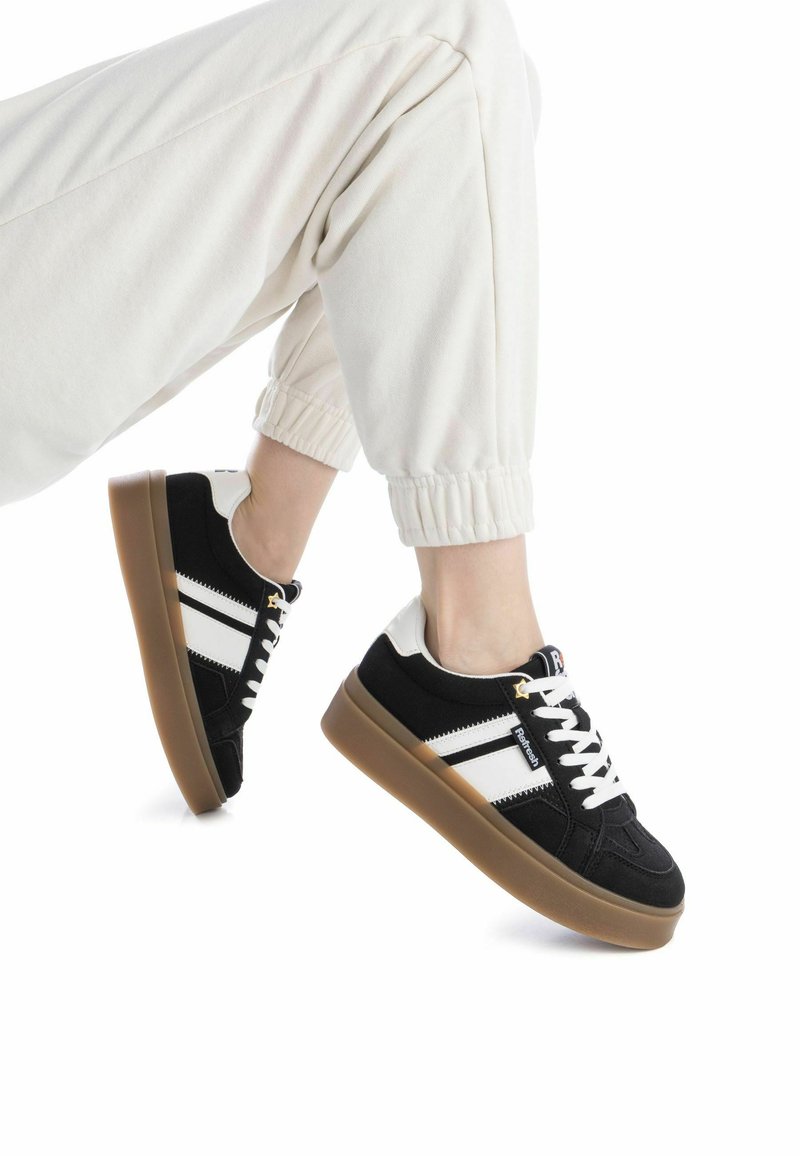 Zapatillas en blanco y negro con una parte superior texturizada, rayas blancas y una suela de goma marrón. Los cordones son blancos y tienen acentos de hardware dorado.