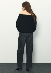 Schwarzer Off-Shoulder-Pullover mit einem gerippten Ausschnitt, kombiniert mit hoch geschnittenen, locker sitzenden Jeans aus dunkelgrauem Denim und schwarzen Stiefeletten mit Absatz.