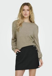 Beige stickad tröja med långa ärmar och ribbade cuffar, i kombination med en svart ribbad minikjol med dekorativa knappar på sidan.