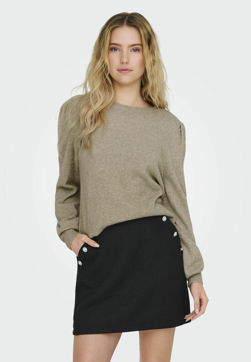 Beige stickad tröja med långa ärmar och ribbade cuffar, i kombination med en svart ribbad minikjol med dekorativa knappar på sidan.