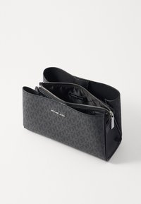 Pochette en tissu noir à motifs avec deux compartiments zippés et bords arrondis. Présente un logo à l'avant et des accents lisses.
