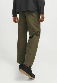Pantalones de pierna ancha de color verde oliva, hechos de tela ligera, combinados con zapatos de ante negros que presentan una suela de goma texturizada.