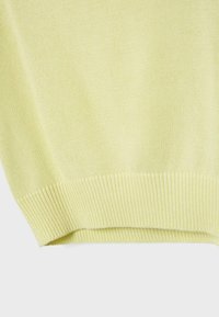 Ourlet de pull tricoté jaune clair avec texture côtelée sur un fond neutre.