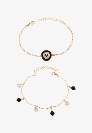 Dwie złote bransoletki z łańcuszka; jedna z zawieszką w kształcie czarno-białego oka proroka, druga z naprzemiennie ułożonymi czarnymi i przejrzystymi koralikami.