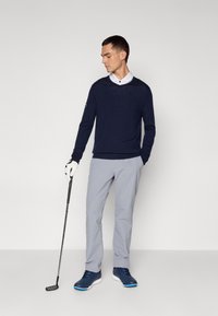 Námořnický pletený svetr, šedé kalhoty a modré sportovní boty; drží golfovou hůl, má na sobě bílou košilí s límečkem a bílou rukavici.