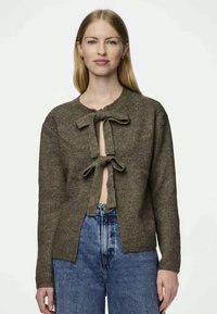 Smeđi pleteni kardigan s kopčanjem na mašnicu, sa širokim izrezom i otvorenim prednjim dijelom. Uparen s farmerkama visokog struka u plavoj boji.