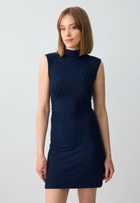 Marineblauwe mouwloze jurk met een gestructureerd patroon, aansluitend ontwerp en hoge hals. De stof lijkt glad met een lichte glans.