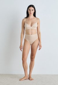 Beige, naadloze bralette en high-waisted slipset, met een minimalistisch ontwerp, dunne bandjes en een zachte, matte textuur.