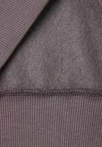 Tessuto grigio con una morbida texture simile al feltro e con un bordo ribattuto. Sutura evidente nella cucitura. Il design complessivo è semplice e funzionale.