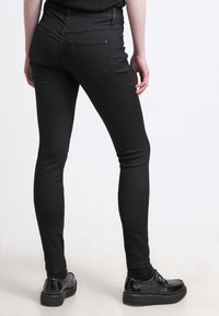 Svarte skinny jeans med en glatt tekstur, som har to baklommer og høy midje. Kombinert med svarte snørestøvler og en enkel topp.