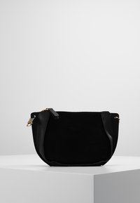 Černá semišová kabelka s kulatým tvarem, disponující zlatými detaily, zipovým uzávěrem a texturovaným povrchem. Kompaktní design vhodný na nezbytnosti.