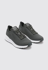 Zapatillas de punto gris con puntera redondeada, suela blanca y cordones a juego. Presentan un logo en el lateral y un cuello acanalado para un ajuste ceñido.