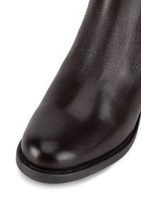 Brūni ādas potītes zābaki ar noapaļotu purngalu, gludu tekstūru un melnu gumijas zoli. Iezīmē minimālu šuvju un elegantu dizainu.