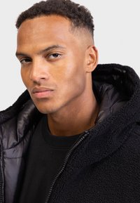 Black hoodie with a plush, textured exterior and a shiny, smooth inner lining. Features a zip closure and adjustable hood.