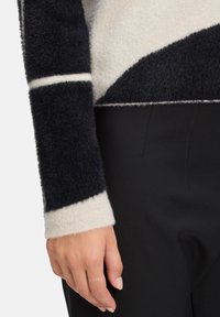 Vluchtige trui met een diagonaal ontwerp in zwart en room; roomkleurige boorden, textiel met wolstructuur, gedragen met zwarte aansluitende broek.