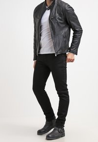Schwarze Lederbikerjacke mit taillierter Passform, kombiniert mit einem weißen T-Shirt, schwarzen Slim-Fit-Jeans und schwarzen Stiefeletten mit einem Schnallenakzent.