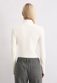 Witte coltrui met lange mouwen, gecombineerd met grijze broek met streepjes. De stof lijkt zacht en nauwsluitend, wat een slanke silhouet benadrukt.