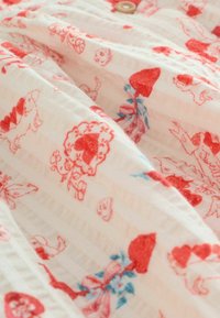 Balts audums ar sarkanu ziedu rakstu, kurā attēlotas zemenes, ziedi un mazi dzīvnieki. Teksturēta virsma ar horizontālām svītrām un koka pogu.