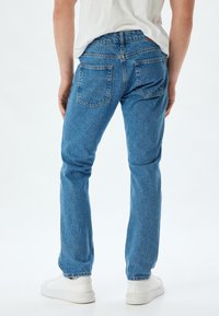 Jeans in denim celeste con vestibilità dritta, design a cinque tasche e leggere sfumature. Indossati con sneakers bianche.