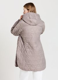 Giacca lunga imbottita con cappuccio in taupe tenue, caratterizzata da un motivo a diamante, texture morbida e slit laterali per facilitare i movimenti.