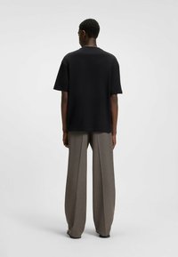 Black short-sleeve t-shirt with a relaxed fit, paired with loose, high-waisted gray trousers, creating a minimalistic silhouette.