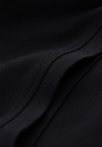 Nahaufnahme von gefaltetem schwarzem Stoff, der eine feine Strickstruktur und glatte, geschwungene Kanten zeigt.