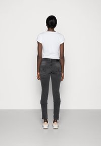 Graue enge Jeans mit Gesäßtaschen, kombiniert mit einem schlichten weißen T-Shirt. Die Jeans haben einen umgeschlagenen Saum und dezente Nähdetails.