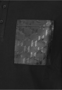 Czarna koszulka polo z teksturowaną czarną skórzaną kieszenią ozdobioną geometrycznym wzorem. Guziki widoczne przy kołnierzyku. Ogólnie gładki materiał.