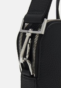 Czarna skórzana torba o teksturowanej powierzchni, srebrnym okuciu, podwójnymi suwakami oraz paskiem z metalowym zapięciem.