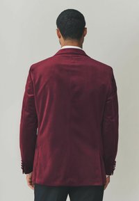 Bordeaux rotes Samtblazer mit glatter Textur, slim fit, mit Reverskragen und geknöpften Manschetten. Maßgeschneiderter Schnitt mit einem Schlitzt hinten.