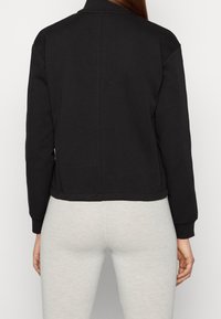 Zwarte cropped sweatshirt met lange mouwen, ribgebreide manchetten en een gladde textuur. Rekbare tailleband en minimale stikdetails.