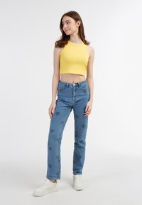 Žlutý žebrovaný crop top spárovaný s světle modrými džíny s vysokým pasem zdobenými srdíčkovými vzory, doplněný bílými teniskami.
