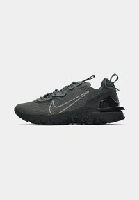 Sneakers Nike in rete grigio scuro con superficie testurizzata, logo riflettente e una suola in gomma nera spessa. Presentano un design con lacci.