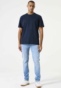 Camiseta de algodón azul marino con cuello redondo y mangas cortas, combinada con jeans azul claro y zapatillas blancas. Diseño simple, sin patrones.