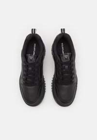 Sorte sneakers med en glat læderoverdel, strukturerede detaljer, snørebånd fortil og en robust sål med fremtrædende trækkrog.