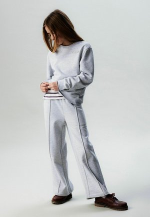 Light grey sweatshirt with ribbed cuffs and "Paris" embroidery, paired with matching light grey pants featuring side seams. Brown shoes complete the look.